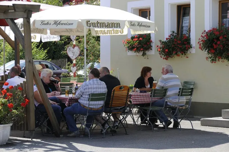 Gäste im Biergarten des Gasthaus Gößwein unter dem Sonnenschirm