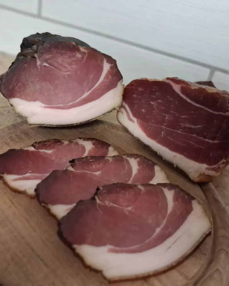 Schwarzgeräucherter Schinken am Stück und dünn aufgeschnitten auf einem Holzbrett