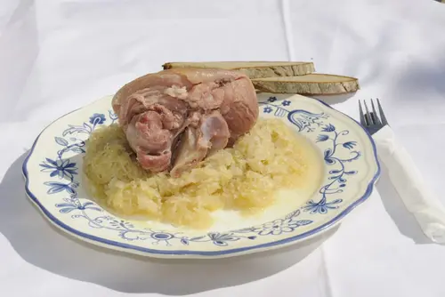 Deftiges Kesselfleisch mit Sauerkraut und Bauernbrot auf blau-weißem Zwiebelmuster-Teller