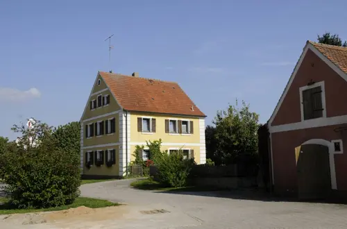 Straßenansicht des Hofs Gößwein mit gelbem Wohnhaus und rotem Nebengebäude
